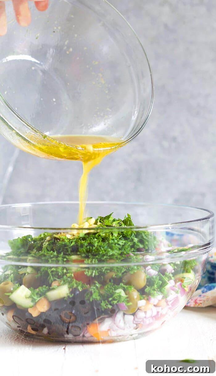 Mediterranean Chickpea Salad with Lemon, Herbs & Feta 7 dressing being poured over chickpea salad in a glass bowl.