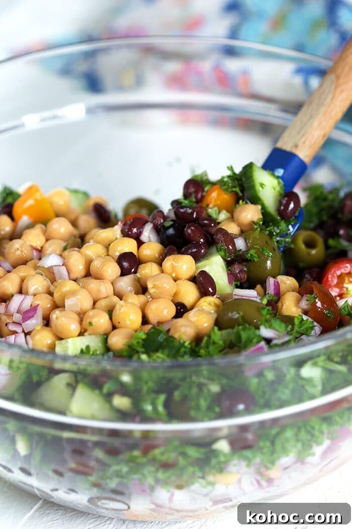 Mediterranean Chickpea Salad with Lemon, Herbs & Feta 8 Ingredients for chickpea salad in a glass bowl with a spatula.