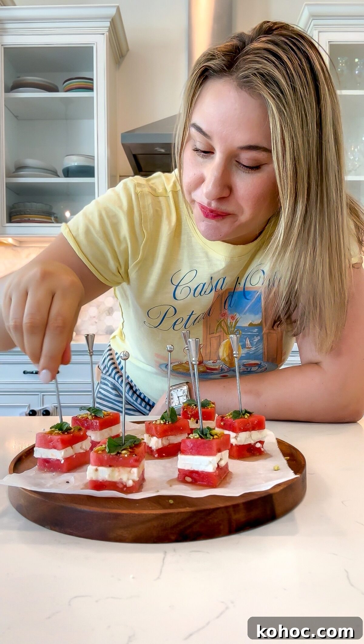 Watermelon Feta Bites with Mint — Refreshing Summer Appetizer 7 Watermelon and Feta Cheese Bites on skewers spread out on a platter with someone about to pick them up.