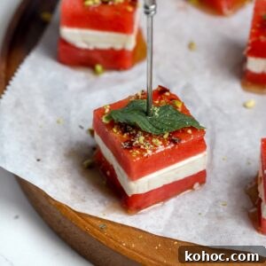 Watermelon and Feta Cheese Bites on skewers spread out on a platter with someone about to pick them up.