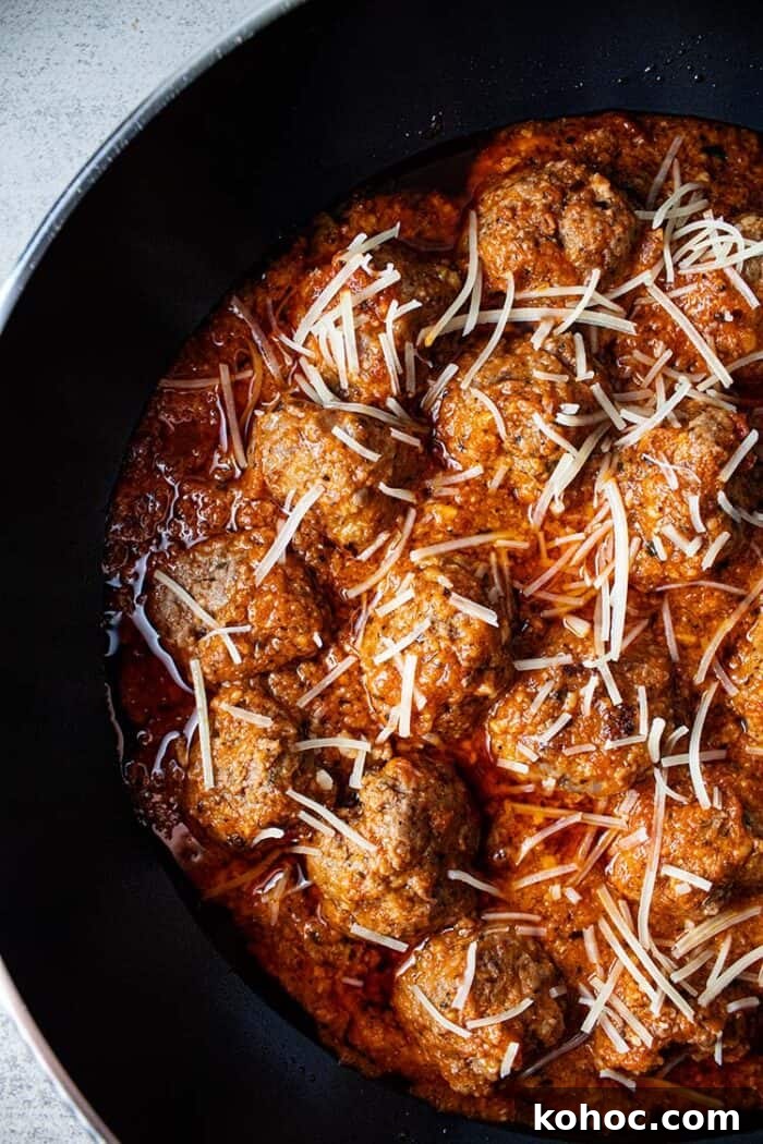 overhead view of keto meatballs with marinara sauce topped with shredded parmesan cheese in a black skillet