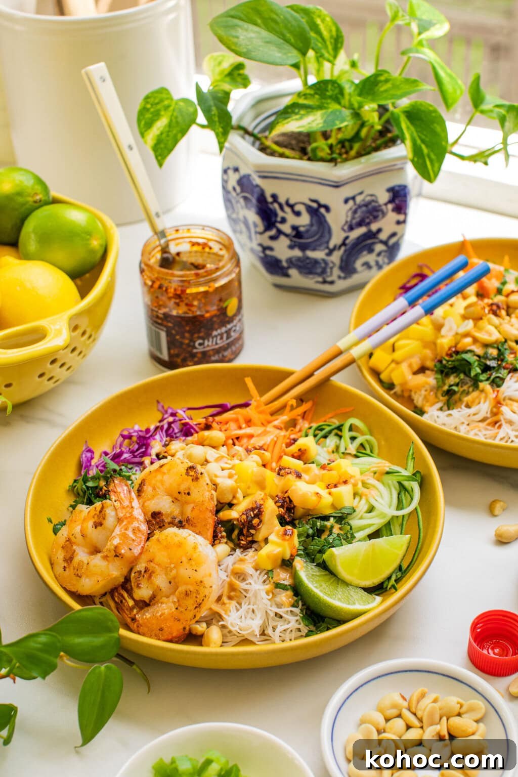 spring roll ingredients in a bowl covered with peanut sauce and grilled shrimp, surrounded by bowls of ingredients and a chili sauce in the background