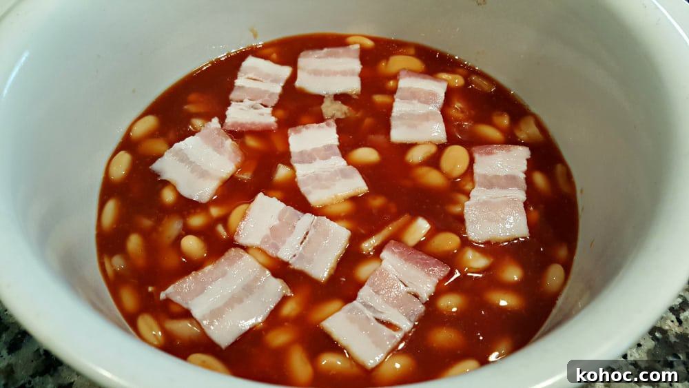 Classic Homestyle Baked Beans Recipe for Comforting Sides 5 bacon pieces layered on top of beans ingredients ready to bake.