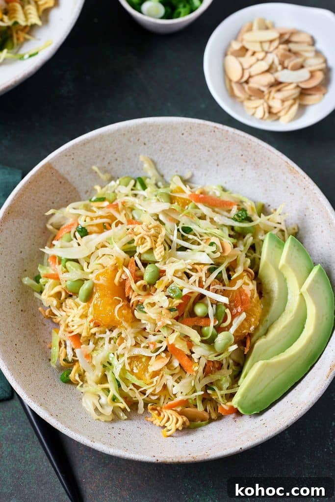Crunchy Ramen Noodle Salad with Cabbage & Almonds 2 Top view of a bowl filled with cabbage slaw, mandarin oranges edamame and crispy ramen noodles tossed and served with slices of avocado.