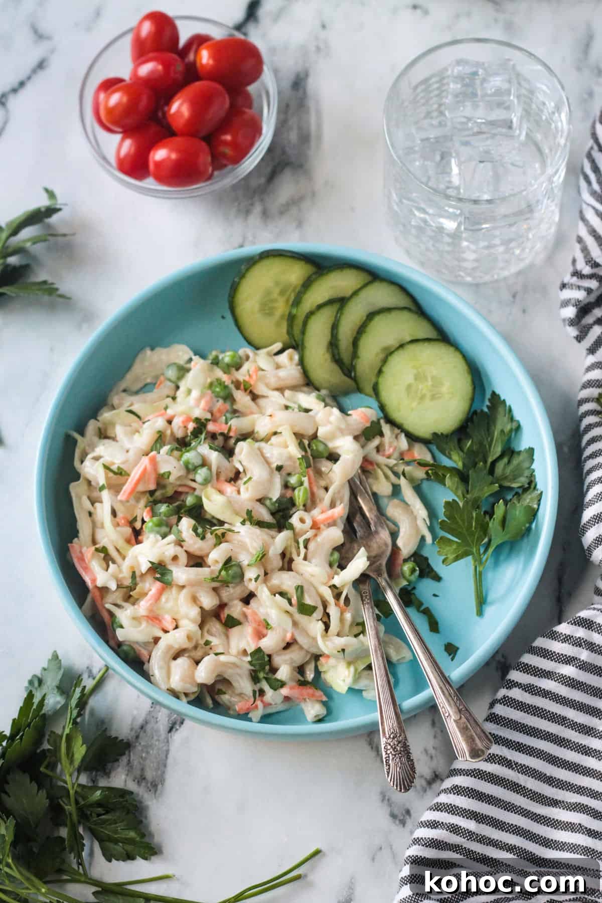 Creamy No-Chop Vegan Macaroni Salad for Quick Meals 2 Vegan Macaroni Salad on a blue plate with two forks and a side of sliced cucumbers.