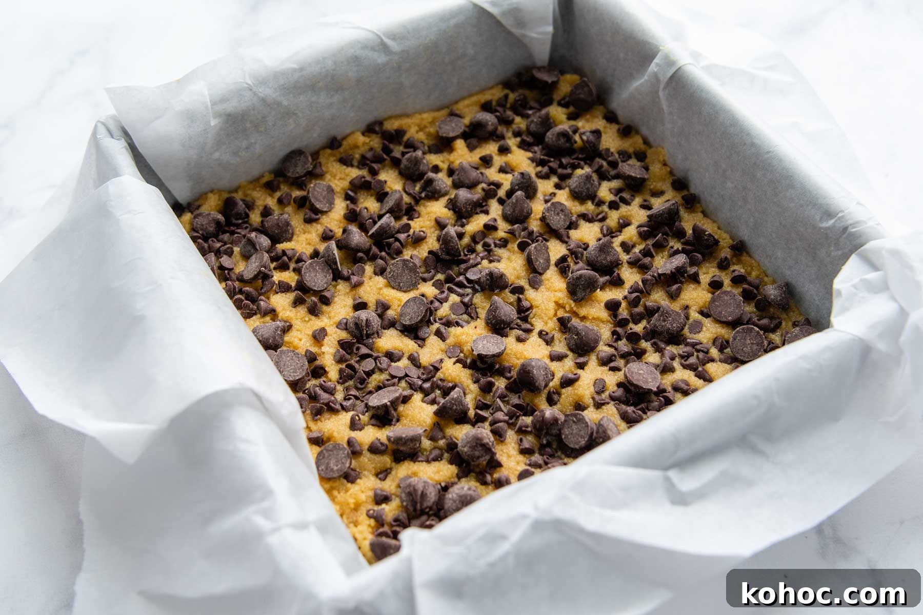 Almond Flour Blondies Recipe – Chewy Gluten-Free Treats 4 an unbaked pan of almond flour blondies with parchment paper overhanging the sides.