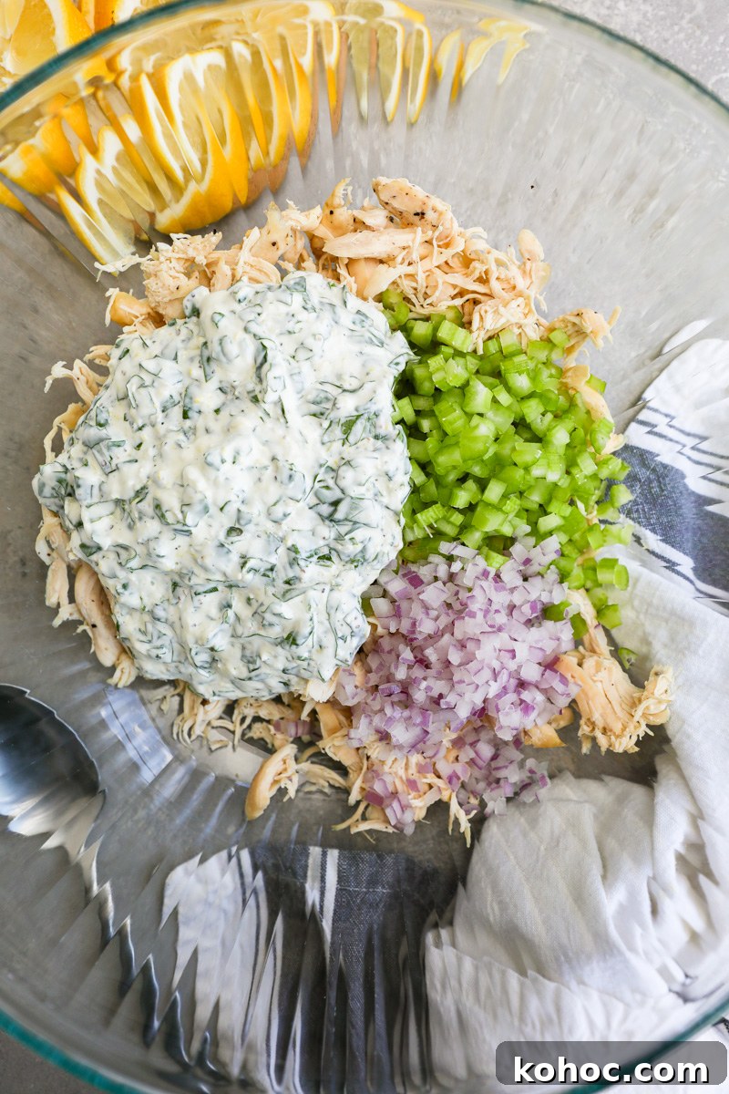 A large clear mixing bowl filled with shredded chicken, diced celery, red onion and a lemon basil "dressing"