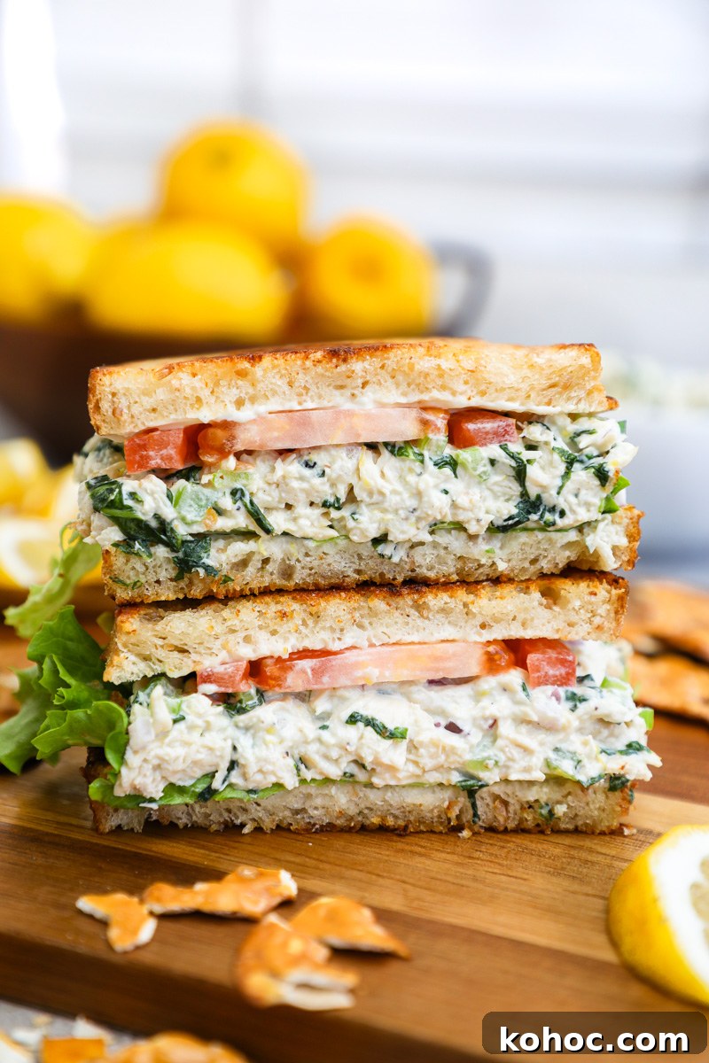 A lemon basil chicken salad sandwich made with lettuce and tomato on toasted bread sitting next to a bowl of lemons
