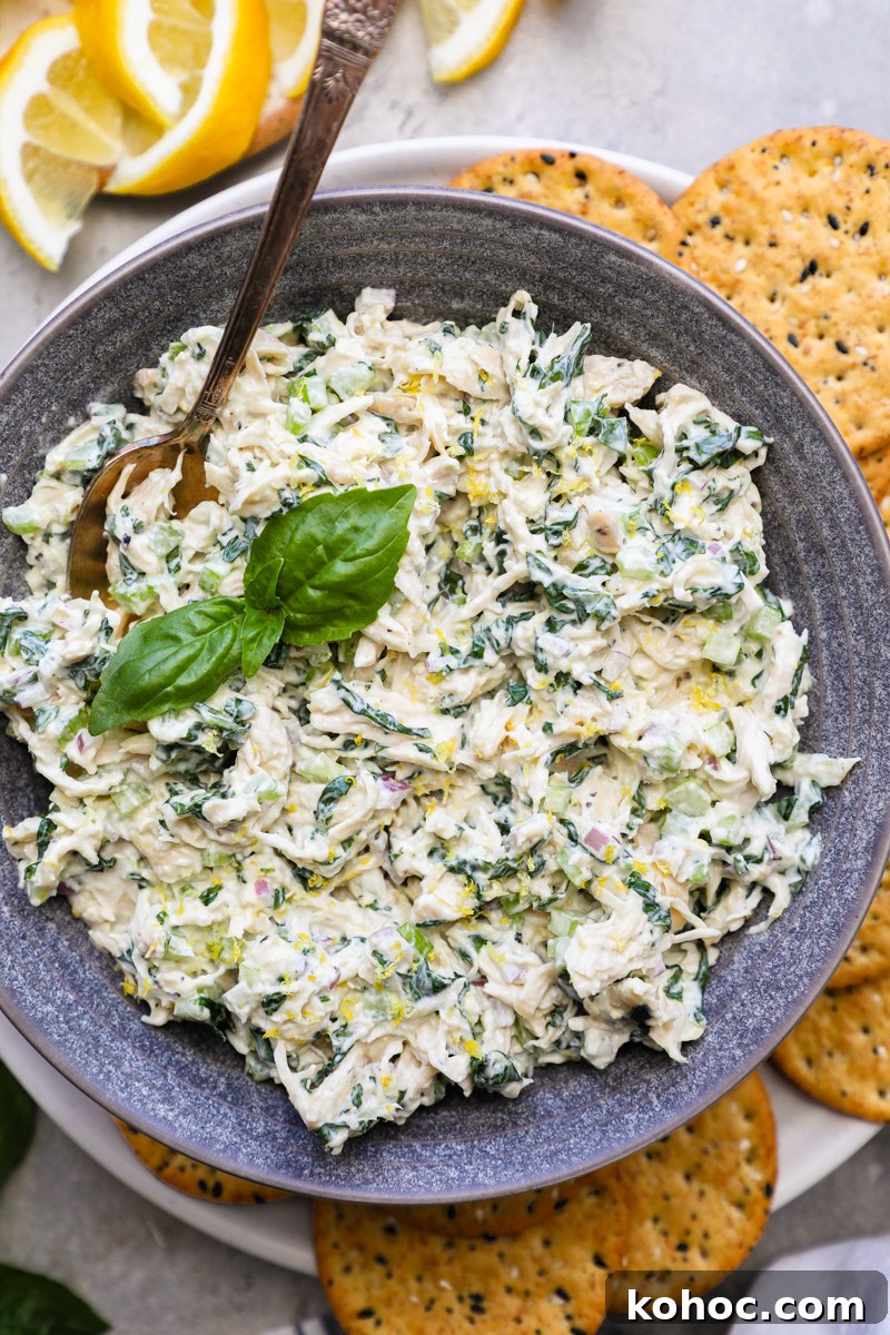 A small serving bowl filled with lemon basil chicken salad surrounded by whole crackers and fresh lemon slices