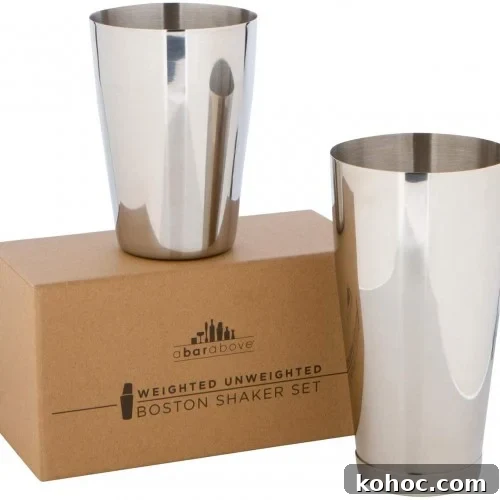 Two stainless steel cocktail shaker tins are shown; one stands upright on a cardboard box, and the other is positioned next to the box. The box is labeled Weighted Unweighted Boston Shaker Set.