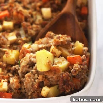 Sausage stuffing in a white baking dish with a wood spoon.