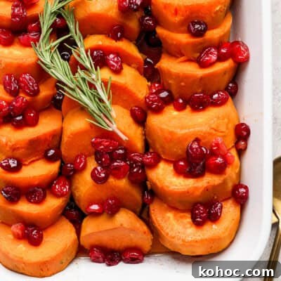 Sliced sweet potatoes topped with cranberries and garnished with a sprig of rosemary, served in a white dish.