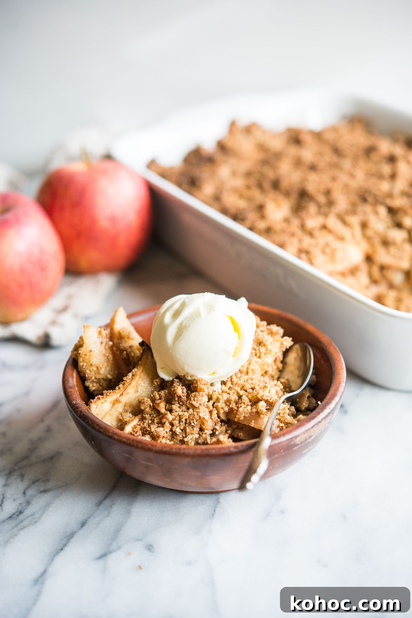 Warm Paleo Apple Crisp with Almond Flour Topping 2 paleo apple crisp in a wooden bowl topped with a scoop of ice cream on a marble surface