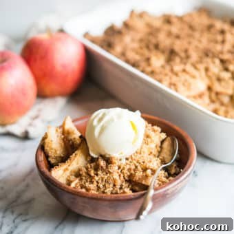 paleo apple crisp in a wooden bowl topped with a scoop of ice cream on a marble surface