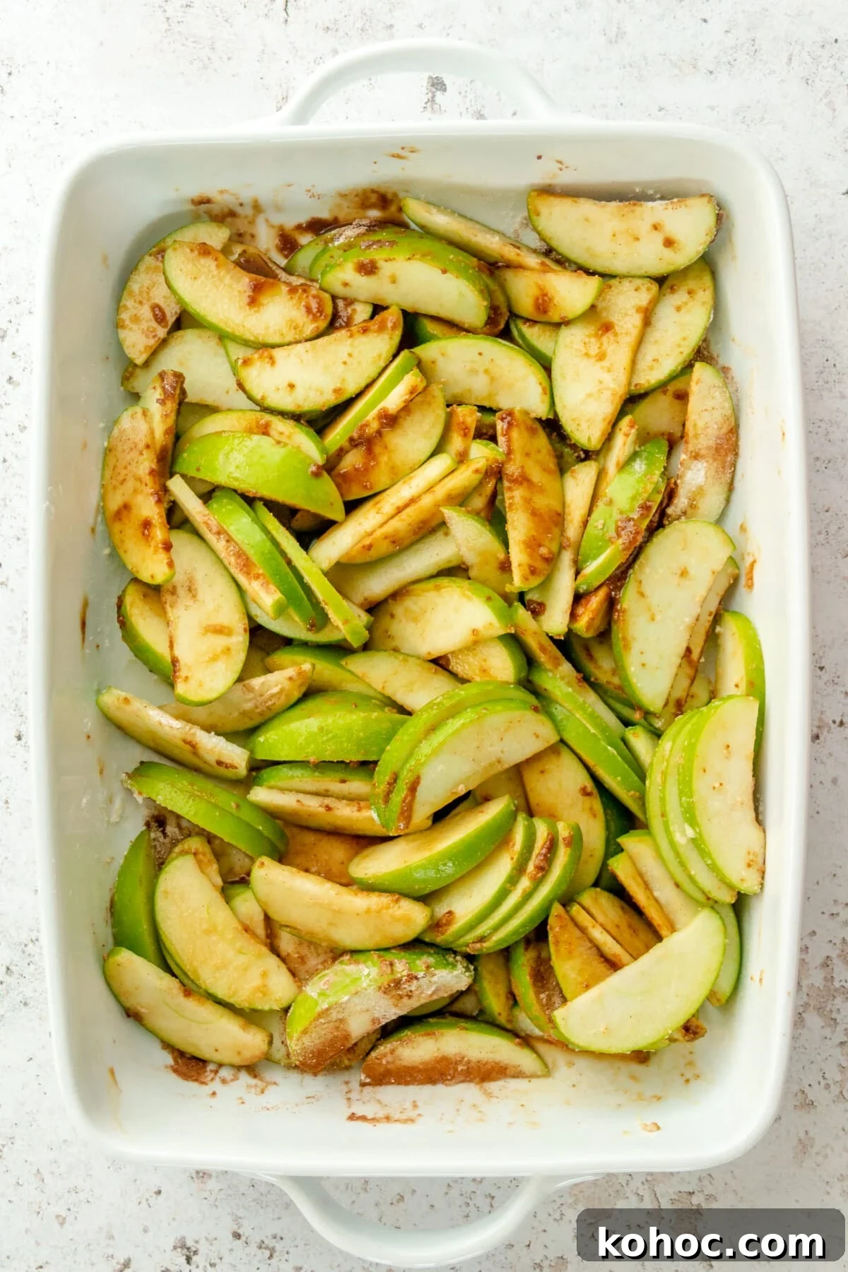 Warm Paleo Apple Crisp with Almond Flour Topping 4 A spiced apple mixture sits in a white ceramic rectangle dish on a light grey surface.