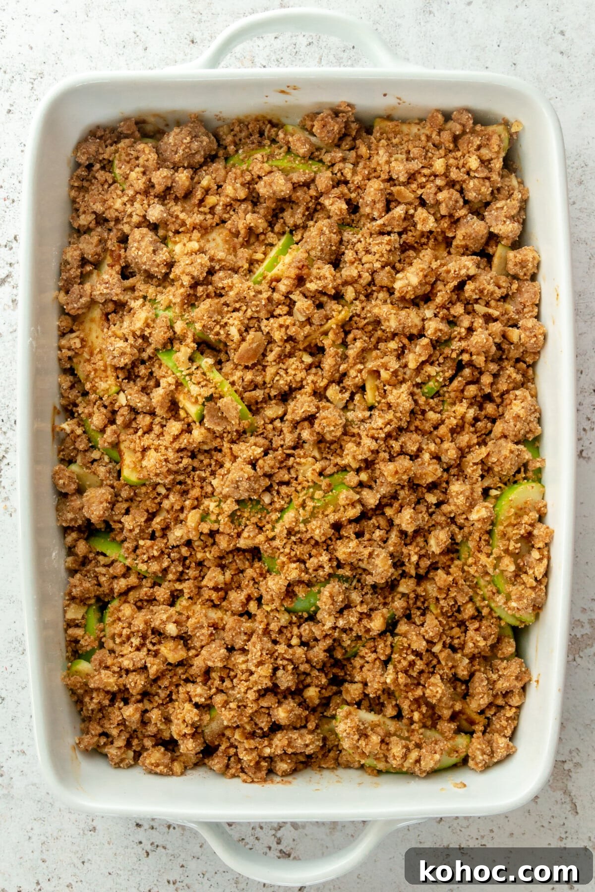 Warm Paleo Apple Crisp with Almond Flour Topping 7 Paleo apple crisp sits in a white ceramic dish prior to baking on a light grey surface.