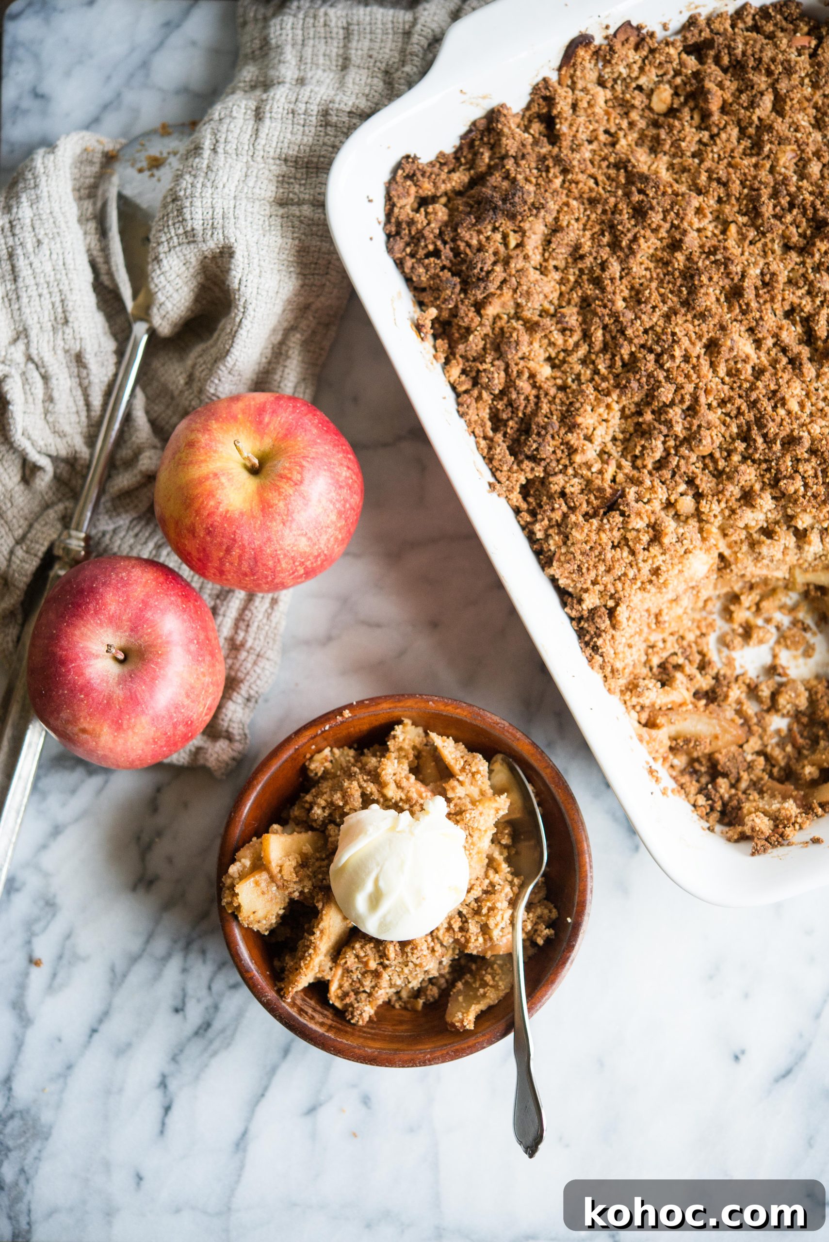 Warm Paleo Apple Crisp with Almond Flour Topping 8 paleo apple crisp in a white rectangular dish with some spooned out into a wooden bowl and topped with a scoop of ice cream
