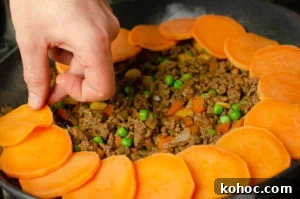 Curried Beef Mince Hotpot Recipe for Comforting Family Dinners 9 Sweet potato slice being placed on top of the mince.