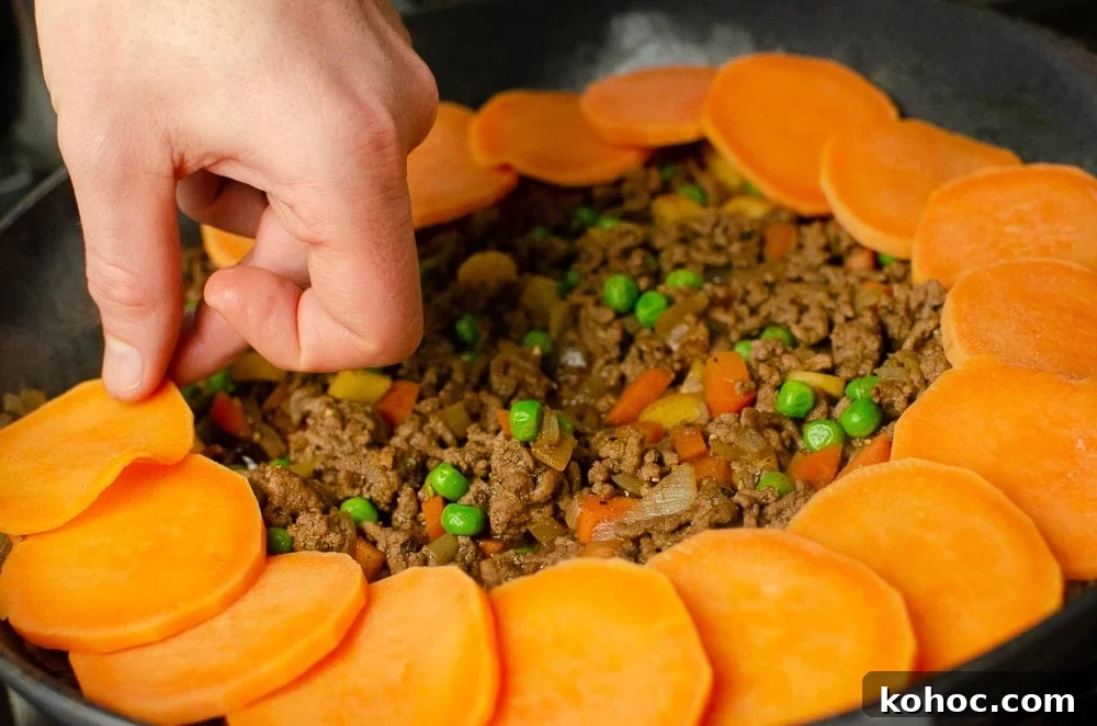Curried Beef Mince Hotpot Recipe for Comforting Family Dinners 21 Sweet potato slice being placed on top of the mince.