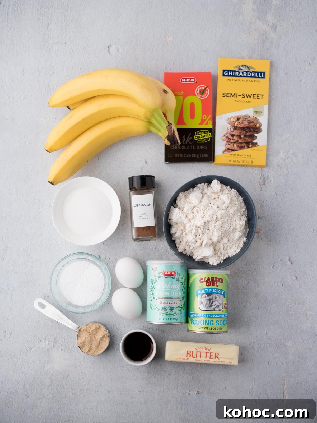 Chocolate Chunk Banana Bread Recipe with Melting Chocolate Chunks 3 Overhead view of ingredients for baking: three bananas, two chocolate bars, bowl of flour, bowl of sugar, cinnamon, salt, two eggs, baking powder, baking soda, brown sugar, vanilla extract, and a stick of butter.