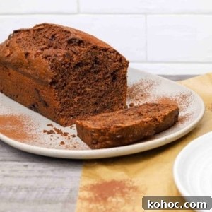 15+ Decadent Chocolate Sourdough Recipes to Try 10 double chocolate sourdough banana bread loaf on a plate with one slice cut, dusted with cocoa powder and served on parchment paper.
