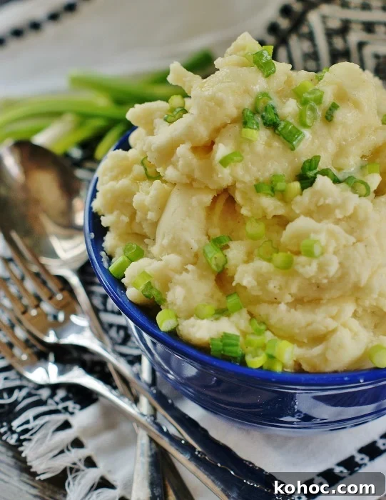 Upclose of a blue Fiestaware serving bowl piled high with horseradish mashed potatoes garnished with chives and drizzled with butter.