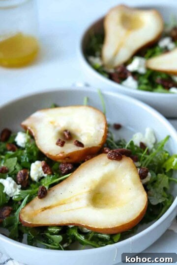 Roasted pear salad in white bowl with honey vinaigrette in jar.