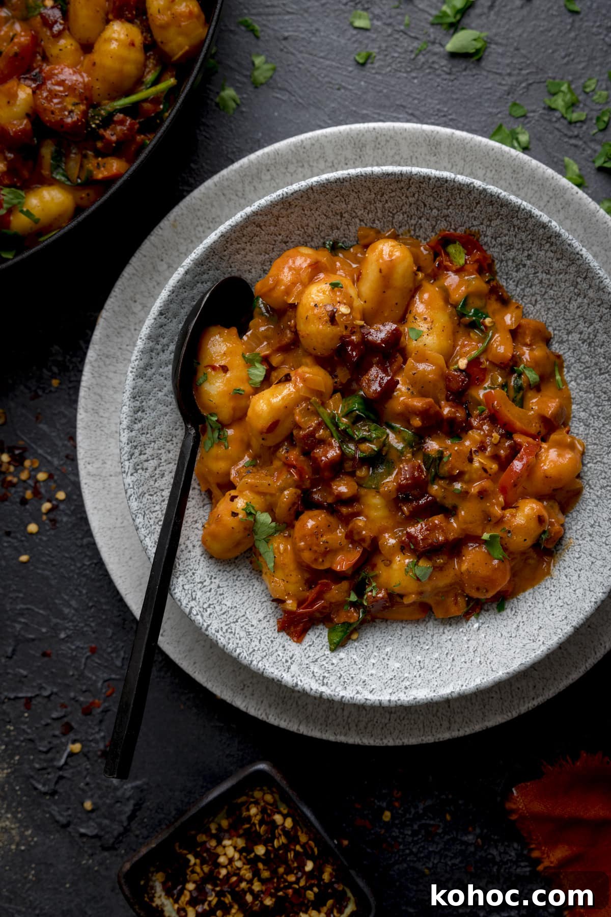 Gnocchi and chorizo in a grey bowl with a black spoon in.