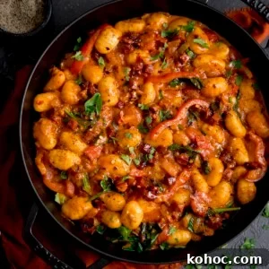 Square image of gnocchi and chorizo in harissa sauce in a black cast iron pan.