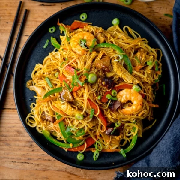 A black plate of stir-fried Singapore noodles with prawns and vegetables.