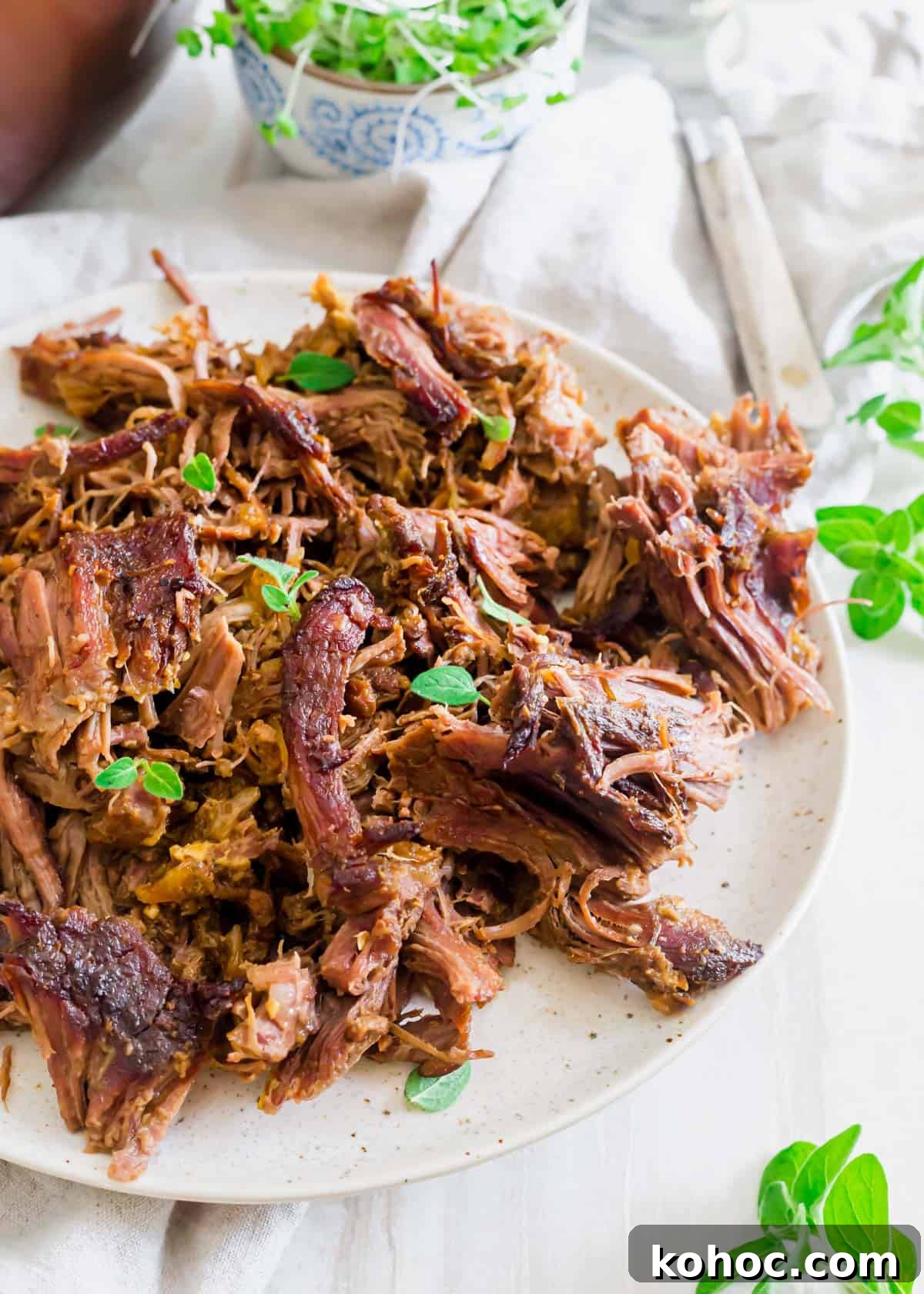 Shredded braised leg of lamb on a plate with fresh oregano can be used in a variety of different lamb dishes. Shredded braised leg of lamb on a plate with fresh oregano can be used in a variety of different lamb dishes.