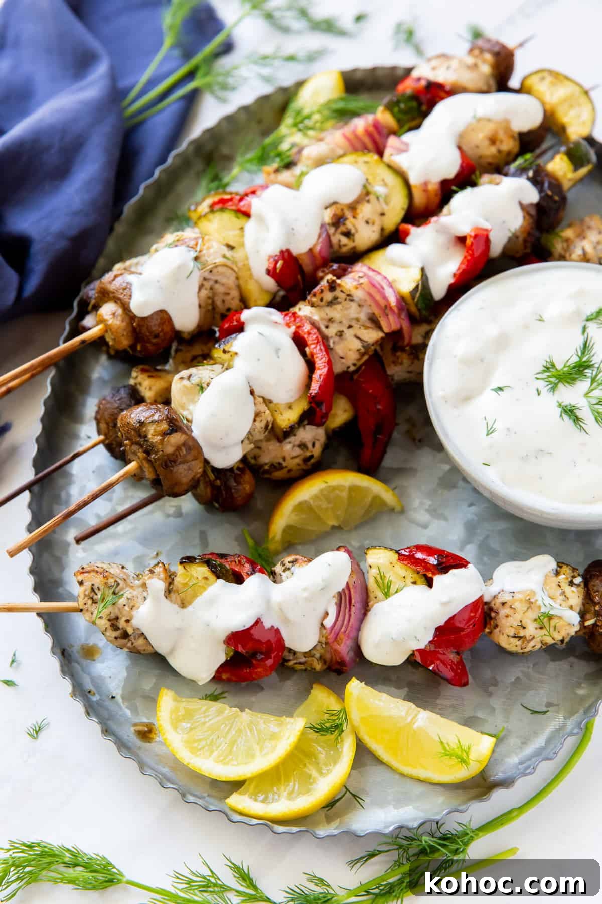 Greek Chicken Kabobs Recipe with Tzatziki and Grilled Vegetables 10 Chicken kabobs with Feta Dill Sauce spooned over the top.