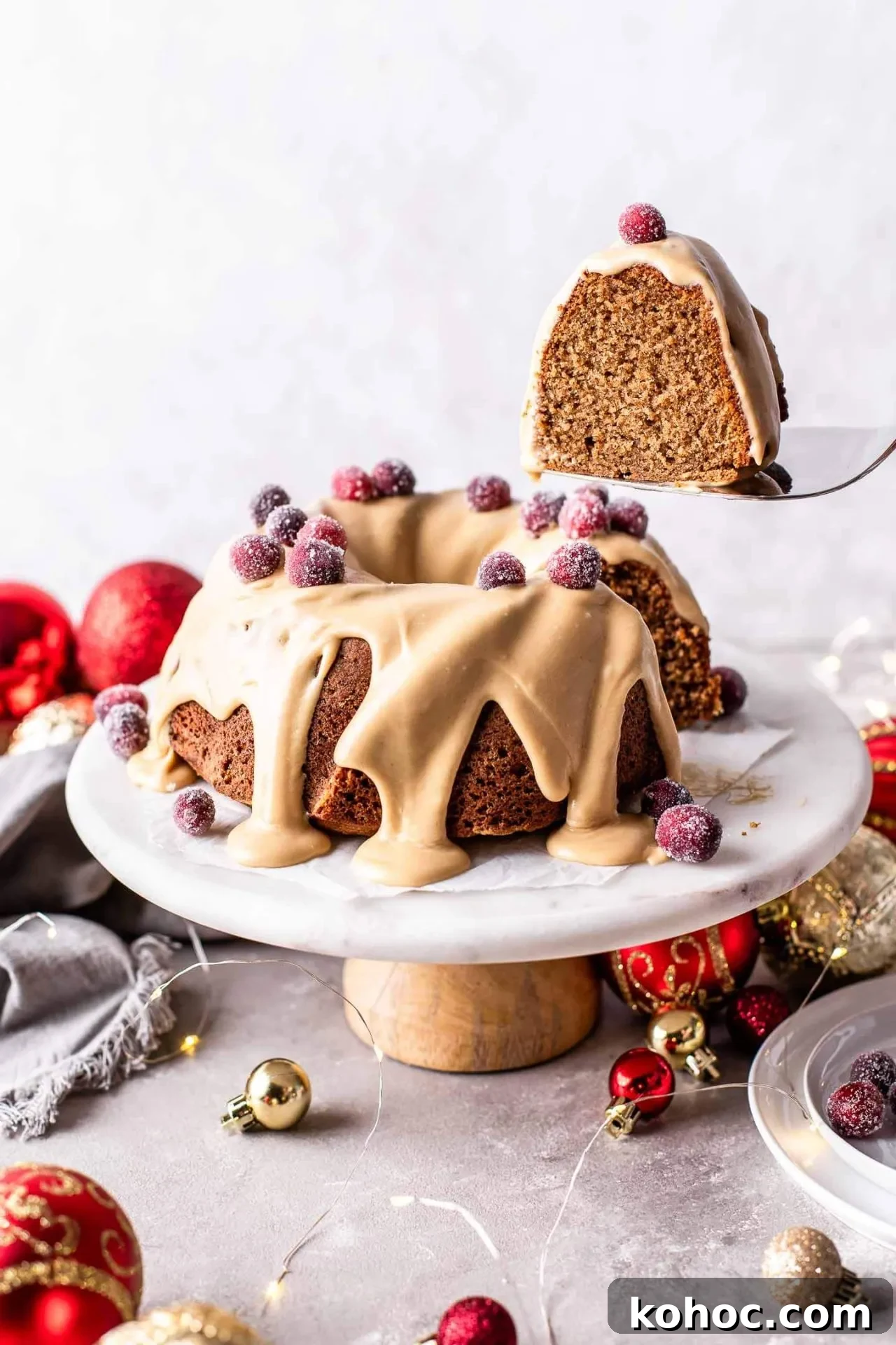 Caramel Gingerbread Cake with Silky Whipped Caramel Icing 11 frosted caramel gingerbread cake decorated with sugared cranberries on cake stand with slice being lifted out on cake server (1)