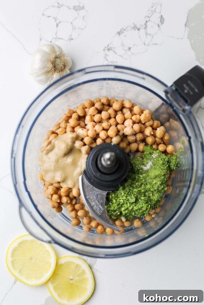 The chickpeas, pesto, and tahini in a food processor bowl.