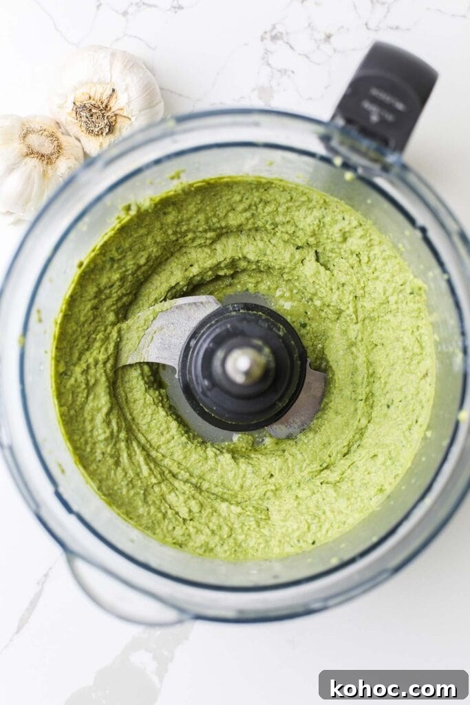 A food processor bowl with a vibrant green pesto hummus.