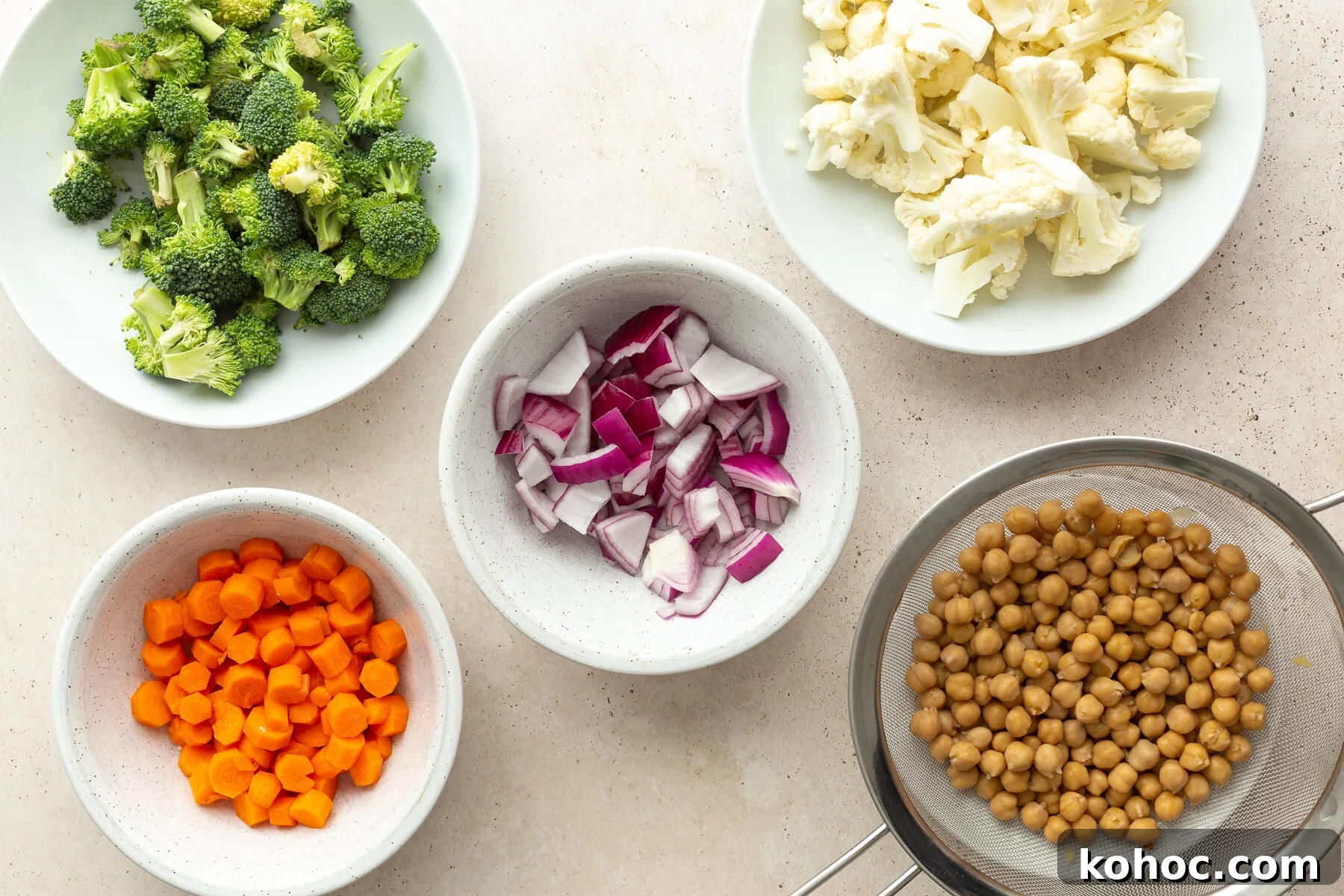 ingredients needed for a roasted veggie bowl: carrots, broccoli, red onion, chickpeas, and cauliflower florets