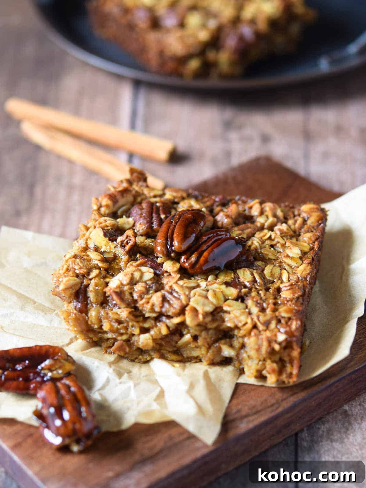 Baked pecan pie oatmeal on a wood slab with cinnamon sticks in the background.