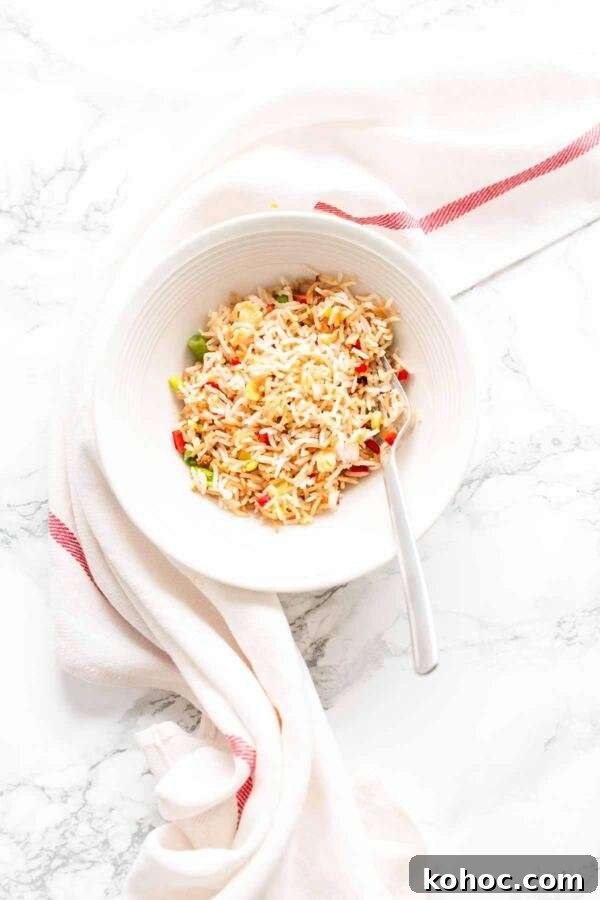 Crispy Air Fryer Fried Rice Recipe for Quick Weeknight Meals 8 Homemade fried rice in a white bowl with a spoon. The fried rice is made in an Air Fryer in no time.
