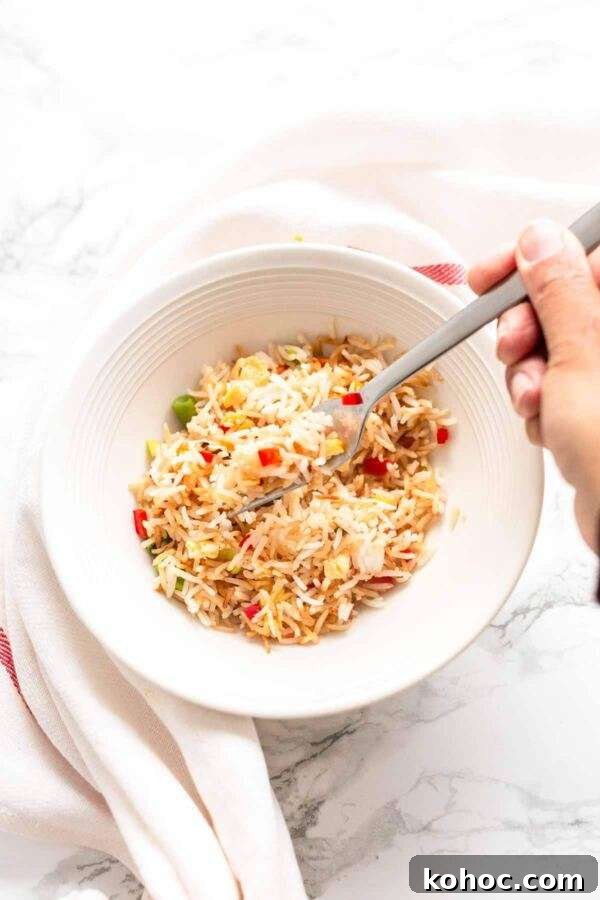 Crispy Air Fryer Fried Rice Recipe for Quick Weeknight Meals 9 Air Fryer fried rice in a white bowl with a spoon. A tasty side dish to serve with dinner.