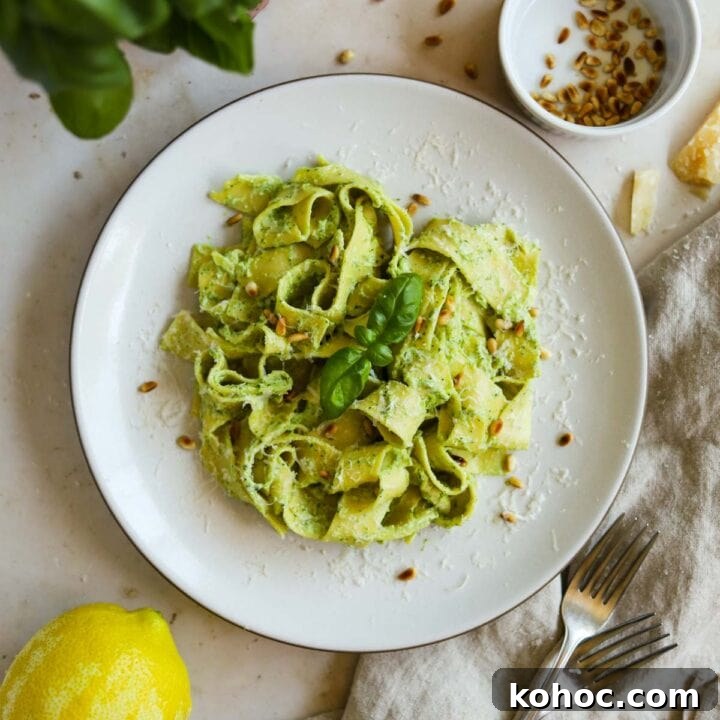 Creamy pesto pasta on a plate with toasted pine nuts and basil.