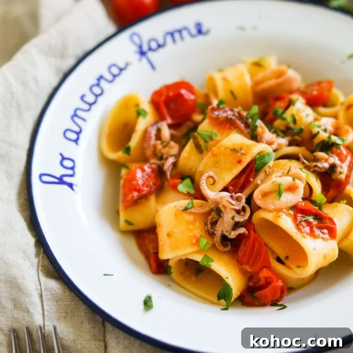 Closeup shot of Calamarata calamari and tomato pasta in a white bowl.