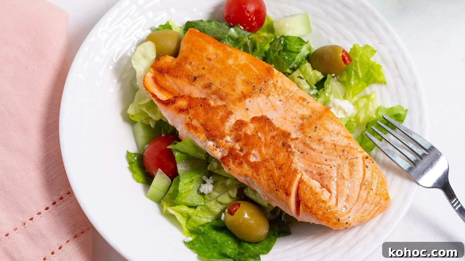 25 Skillet Meals Ready in 30 Minutes or Less 14 A grilled salmon fillet served on a bed of fresh salad with lettuce, tomatoes, and olives on a white plate.
