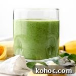 A glass with a green breakfast smoothie in it on a surface with bananas and spinach in the foreground and background.