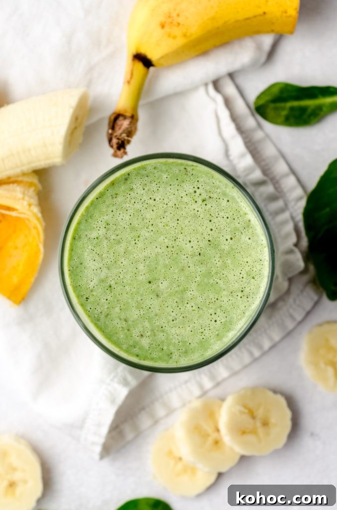 Aerial photo of a green breakfast smoothie on a surface with bananas and spinach around it.