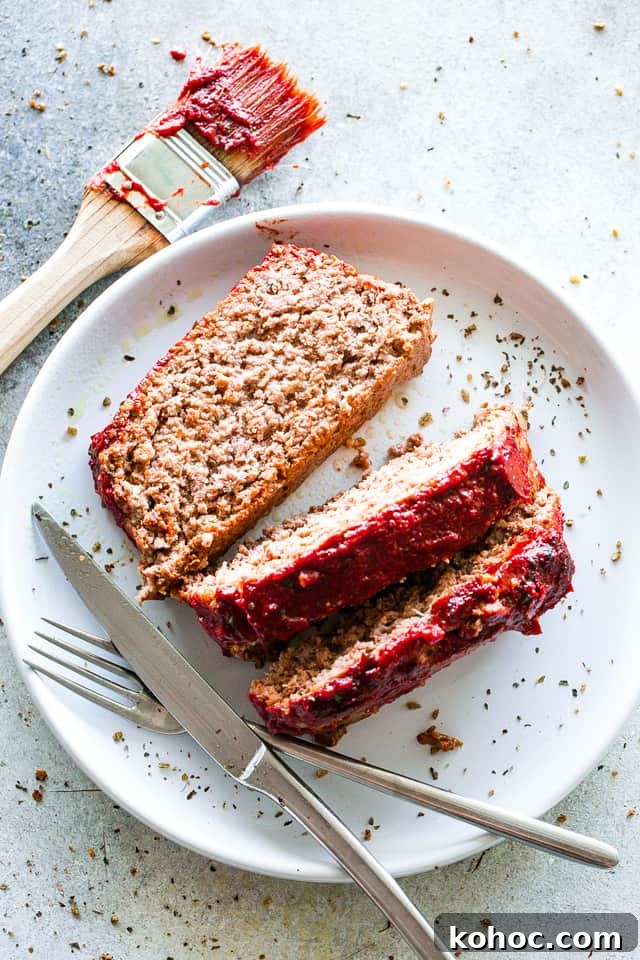 Make this juicy yet easy meatloaf recipe with a ketchup glaze, prepared with ground beef chuck and stuffed with cheese—it’s irresistibly good! Sliced meatloaf on a white plate with a fork and knife
