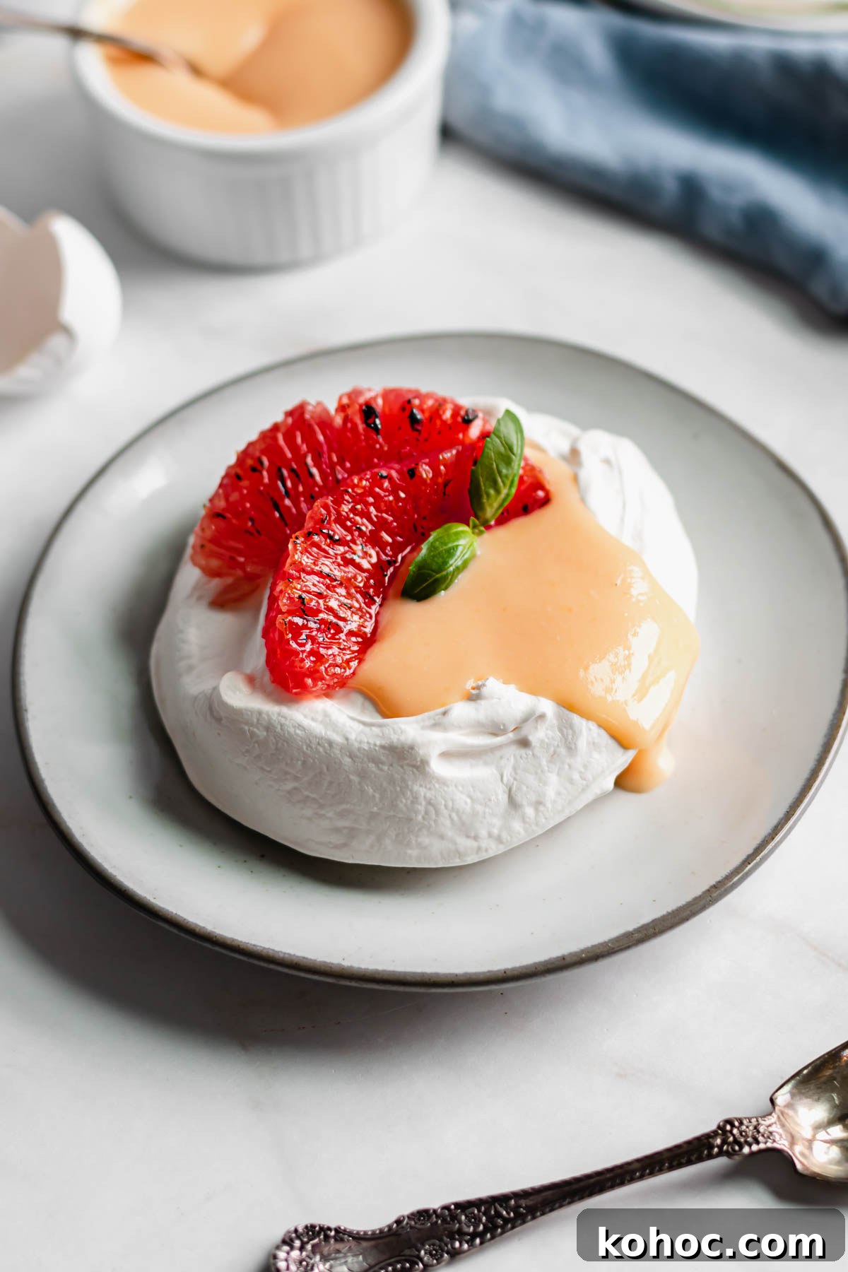 Individual pavlova filled with grapefruit curd and two slices of grapefruit. The curd drips over one side.