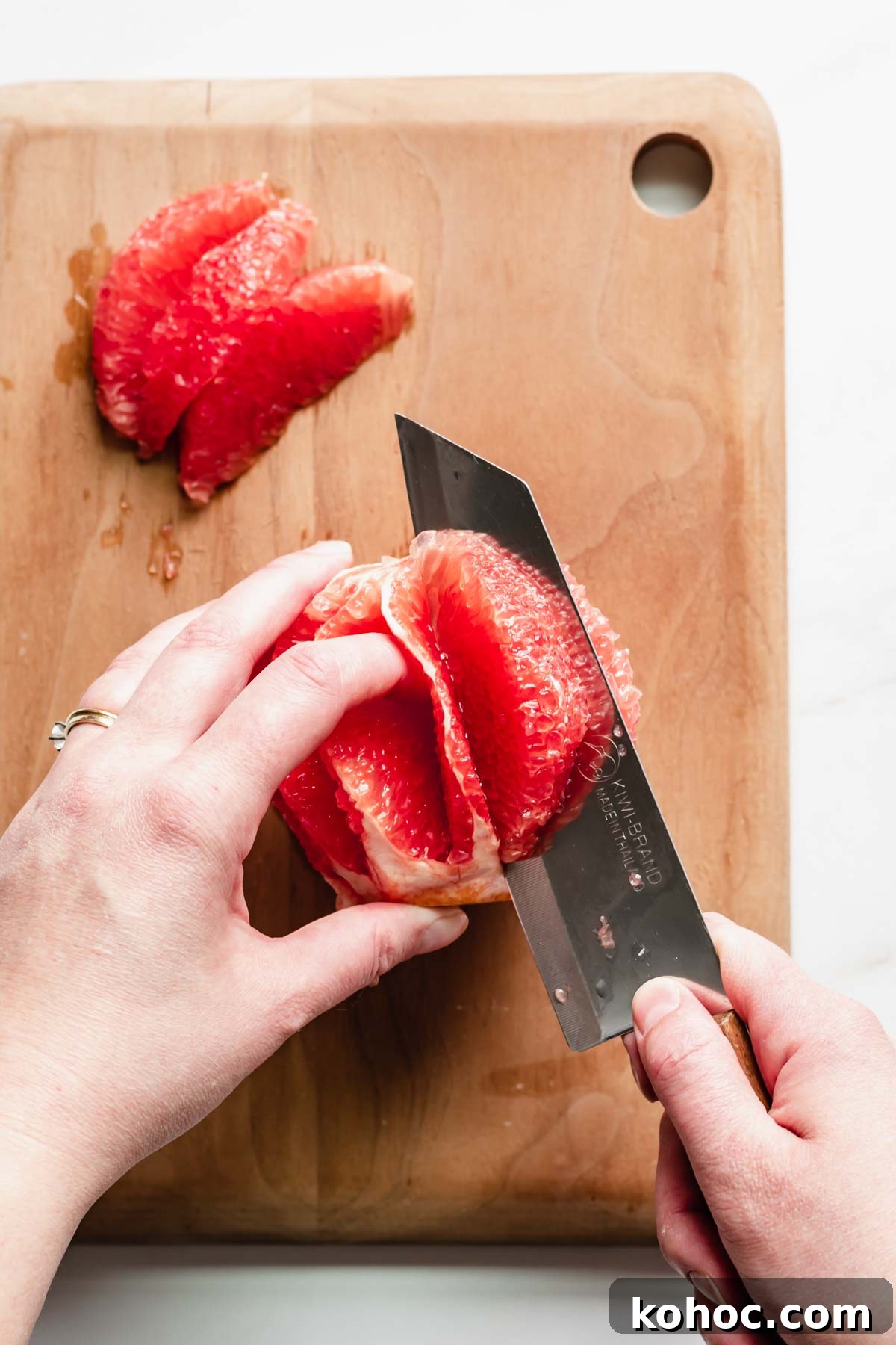 A knife cuts into a segment of grapefruit to create a garnish.