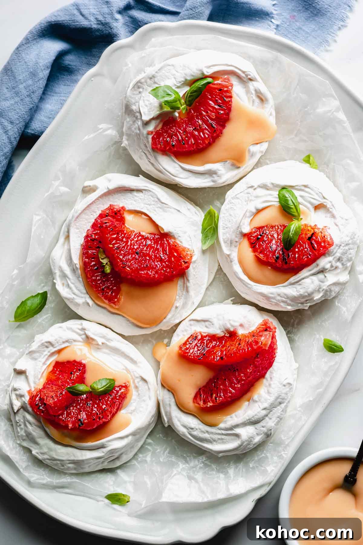 A platter with five assembled mini pavlova nests. Small pieces of basil garnish the platter.