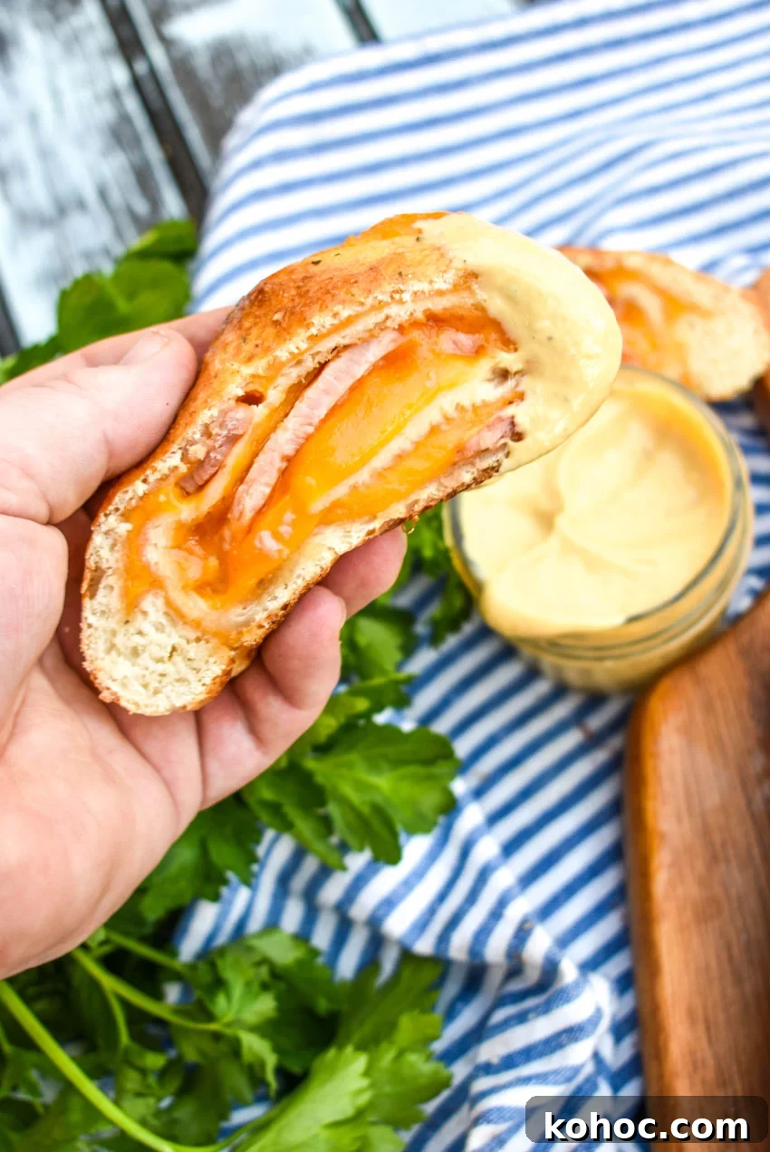 Ham and Cheese Stromboli Recipe: Crispy, Melty and Simple 6 a hand holding up a slice of baked stromboli that's been dipped in honey mustard sauce