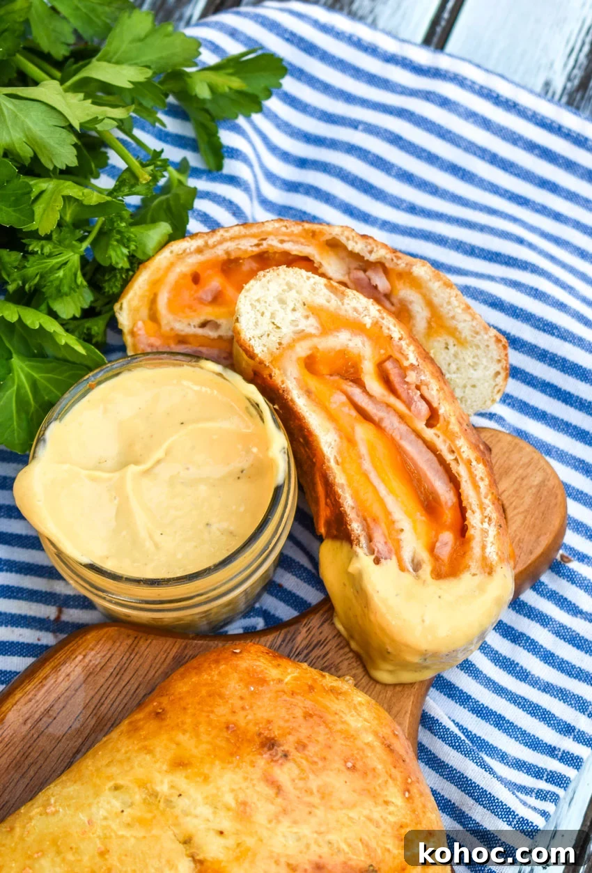 Ham and Cheese Stromboli Recipe: Crispy, Melty and Simple 7 a honey mustard dipped slice of baked stromboli with ham resting on a wooden cutting board